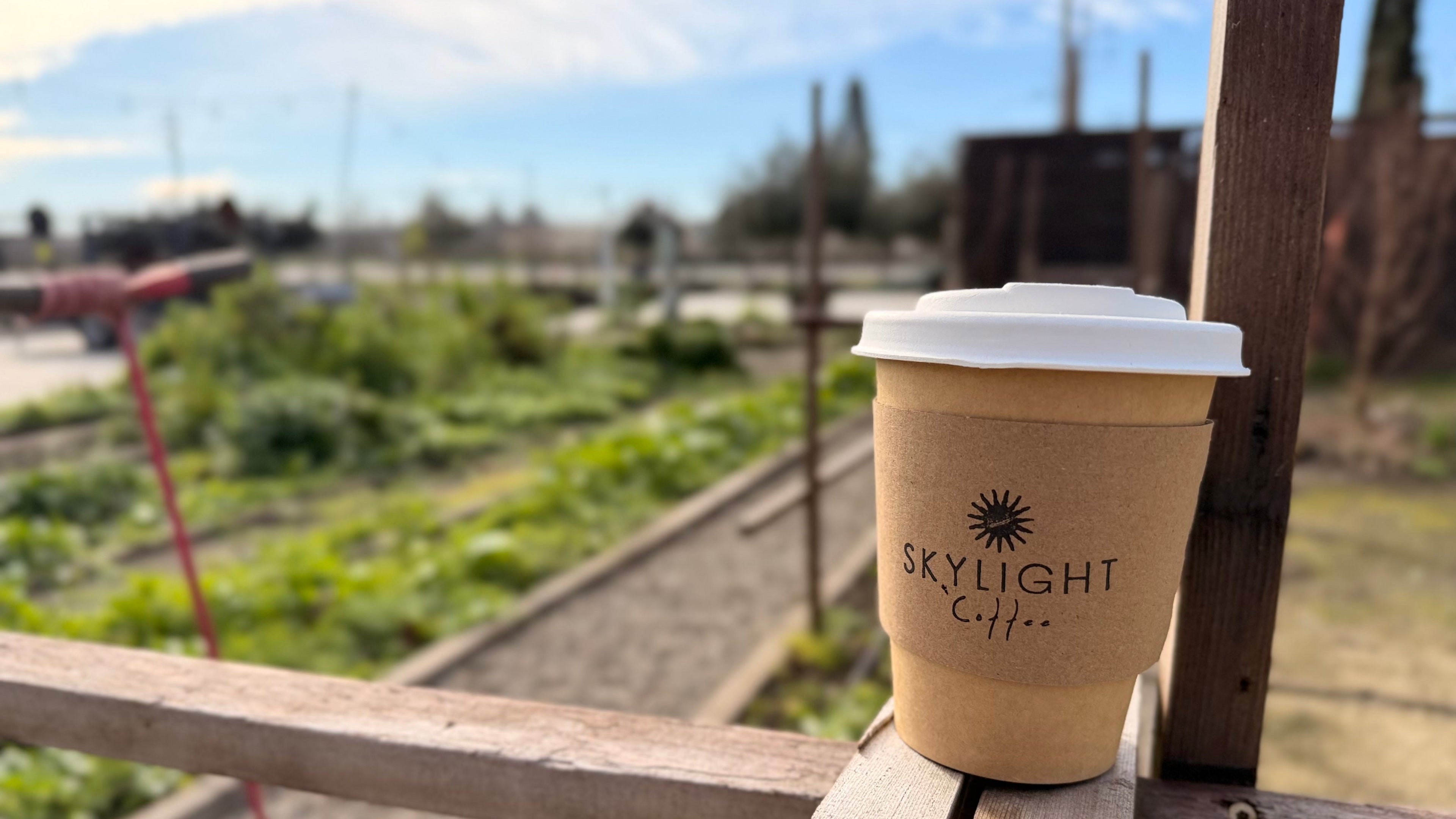 Skylight Coffee cup on a wooden railing with a garden and blue sky in the background